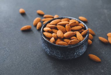 Koyu arkaplanda sağlıklı bademler olan bir kase