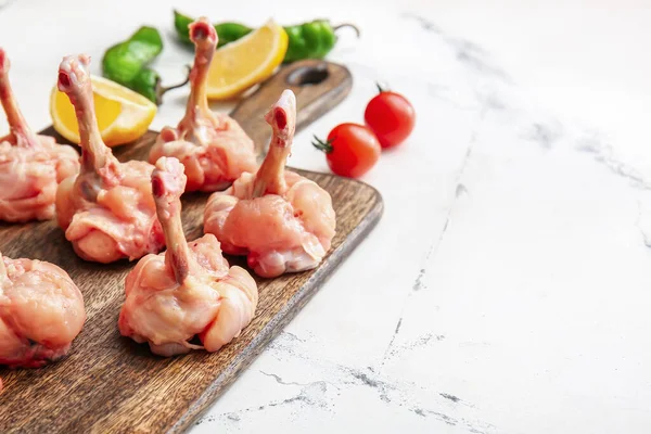 Board with raw chicken lollipops on light background