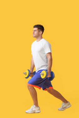 Renkli arka planda dambılları olan sportif genç adam eğitimi.