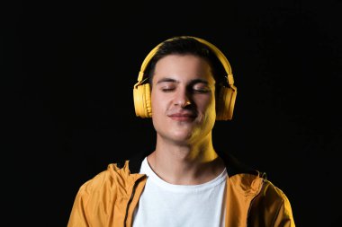 Yakışıklı genç adam karanlık arka planda müzik dinliyor.