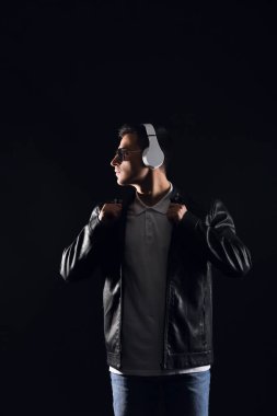 Yakışıklı genç adam karanlık arka planda müzik dinliyor.