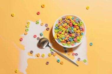 Renkli mısır gevreği halkaları, kaşık ve sütle dolu bir kase.