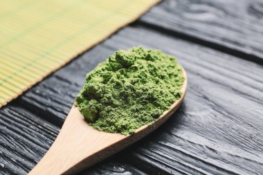 Koyu ahşap arka planda toz kibrit çayı ile kaşık.