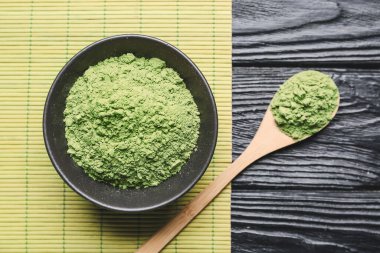 Koyu ahşap arka planda pudralanmış kibrit çayı ile kase ve kaşık.