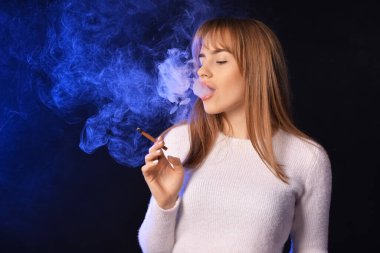 Siyah arka planda sigara içen genç bir kadın.