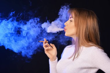 Siyah arka planda sigara içen genç bir kadın.