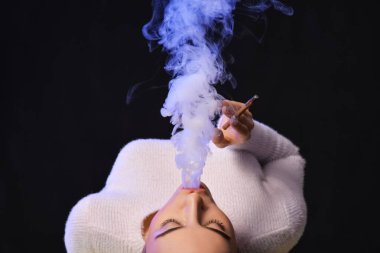 Siyah arka planda sigara içen genç bir kadın.