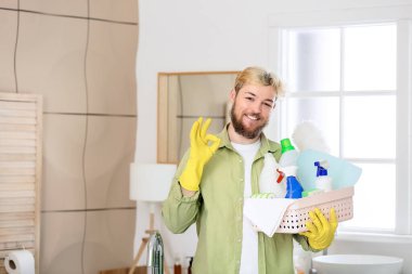 Temizlik malzemesi taşıyan genç adam banyoda iyi görünüyor.