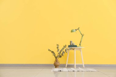 Odasında lamba ve renkli duvarın yanında kitaplar olan masa.