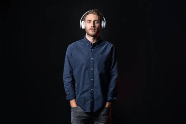 Yakışıklı genç adam karanlık arka planda müzik dinliyor.