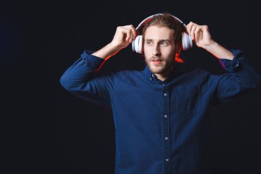 Yakışıklı genç adam karanlık arka planda müzik dinliyor.