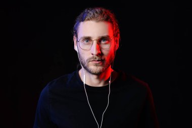 Yakışıklı genç adam karanlık arka planda müzik dinliyor.