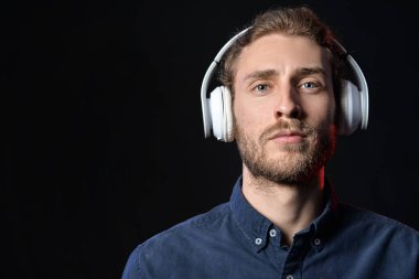 Yakışıklı genç adam karanlık arka planda müzik dinliyor.