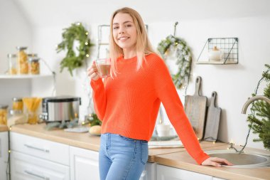 Güzel genç bir kadın Noel arifesinde evde sıcak çikolata içiyor.