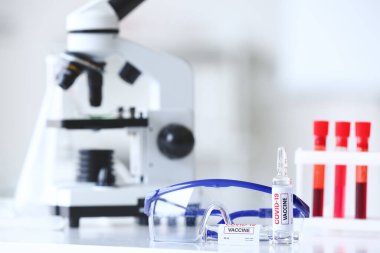 COVID-19 'a karşı yapılan aşı örnekleri ve laboratuvardaki masada duran gözlükler.