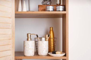 Işık duvarının yanında banyo aksesuarları olan şık raf ünitesi.