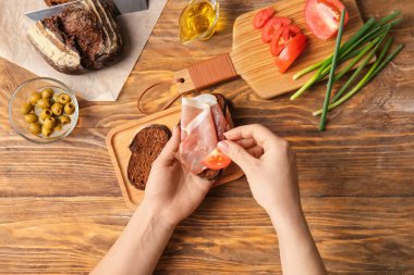 Kadın masada jambonlu ve domatesli sandviç hazırlıyor.