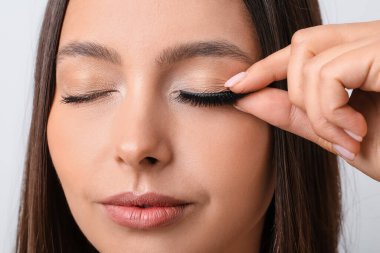 Güzel genç bir kadın arka planda sahte kirpiklerini takıyor.