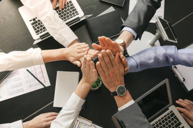 İş adamlarından oluşan bir ekip ofiste el ele tutuşuyor.