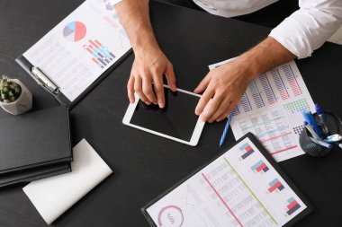 Ofisteki karanlık masada tablet bilgisayarla çalışan genç işadamı.