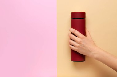 Renkli arka planda modern termosu olan kadın eli