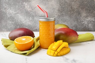 Bir bardak taze mango suyu ve arkaplanda meyveler.