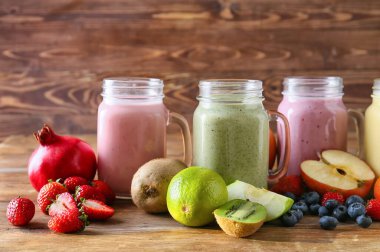 Lezzetli meyveli mason kavanozları ve ahşap arka planda çilekli smoothie.