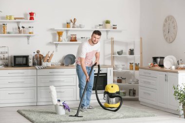 Genç adam mutfakta süpürge yapıyor.