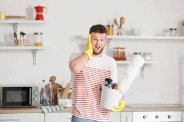 Mutfakta temizlik malzemeleriyle şaşırmış genç bir adam.