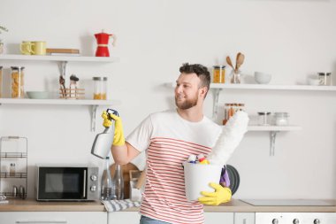 Mutfakta temizlik malzemesi olan genç bir adam.