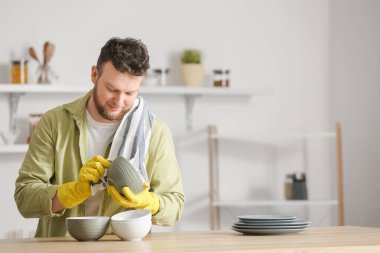 Genç adam mutfakta masaları siliyor.