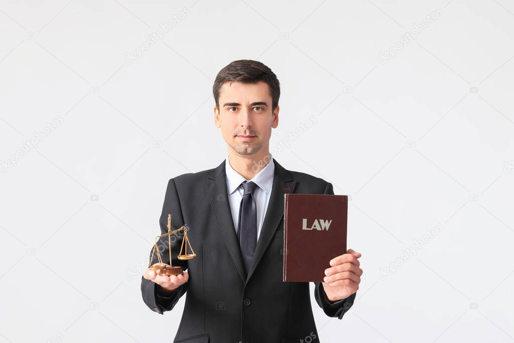 Male lawyer with book and scales of justice on grey background