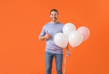 Balonlu yakışıklı genç adam, arka planda başparmağını kaldırıyor.