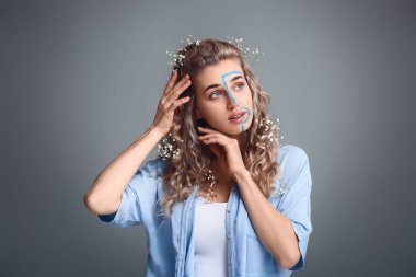 Gri arka planda boyalı yüzü olan güzel genç bir kadın.