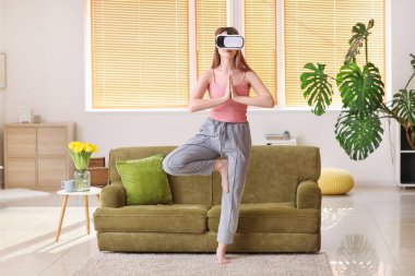 Sanal gerçeklik gözlüklü genç kadın evde yoga yapıyor.