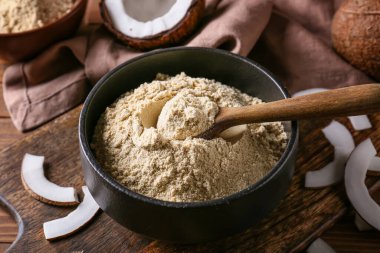 Tahta arka planda hindistan cevizi unu ve kaşıkla kase.