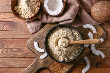 Tahta arka planda hindistan cevizi unu ve kaşıkla kase.