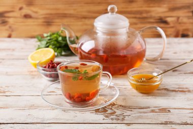 Ahşap zemin üzerinde goji çayı olan bir fincan ve çaydanlık.