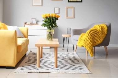 Odanın içindeki masanın üzerinde güzel sarı güller olan vazo.