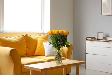 Odanın içindeki masanın üzerinde güzel sarı güller olan vazo.