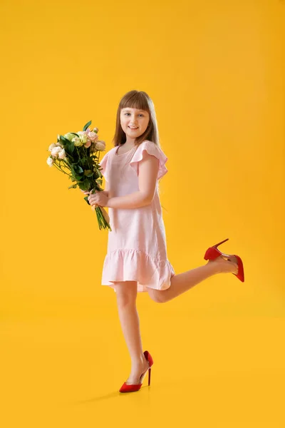 Cute little girl with mother\'s shoes and bouquet of beautiful flowers on color background