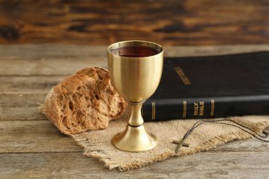 Kutsal İncil ve ahşap zemin üzerinde ekmek olan bir kadeh şarap.
