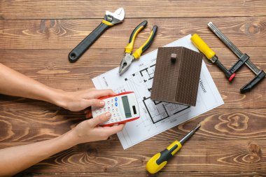 Ahşap arka planda ev modeli ve inşaat aletlerine sahip kadın elleri