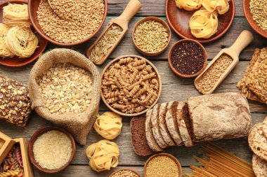Tahta zemin üzerinde farklı tahıllar, çiğ makarna ve ekmek.