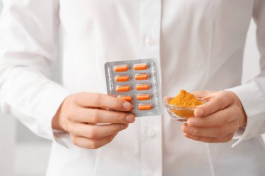 Kadın doktor elinde bir paket zerdeçal hapı ve toz tutuyor.