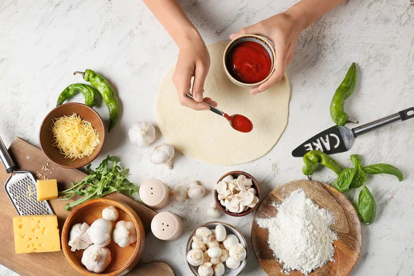 Kadın arka planda pizza yapıyor.