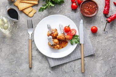 Lezzetli tavuklu lolipoplar ve gri arka planda domatesler.