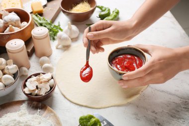 Kadın arka planda pizza yapıyor.