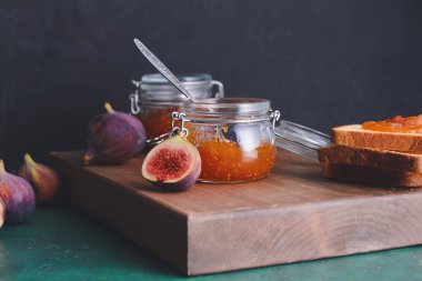 Glass jars with sweet fig jam on dark background