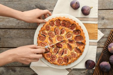 Woman cutting delicious fig pie on wooden background